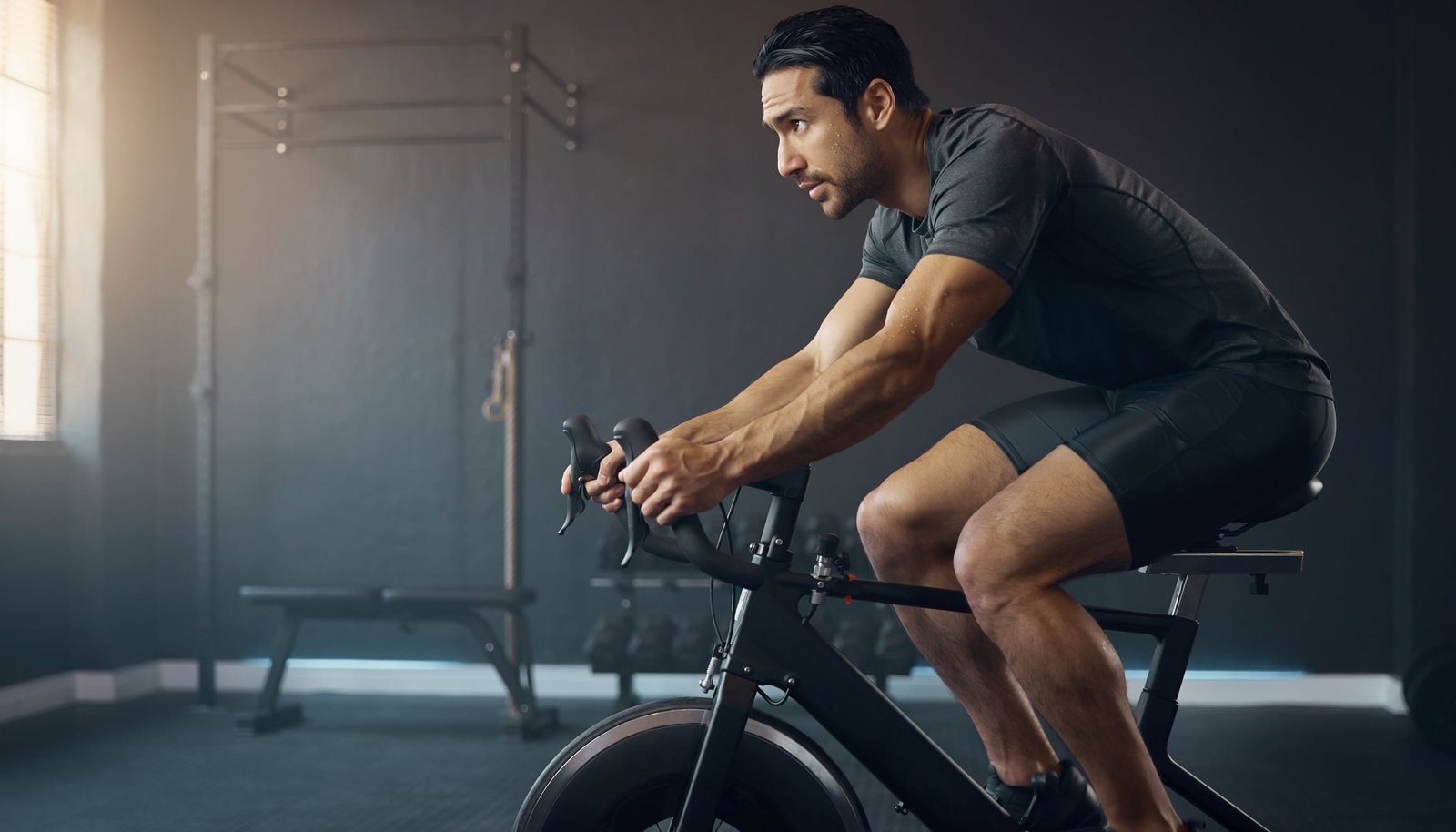 Man training on a modern stationary exercise bike in a premium home gym with weights and workout equipment nearby