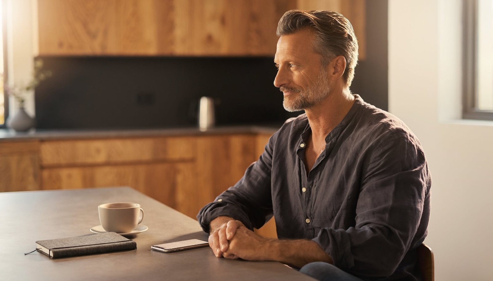 Man calmly looking away from a smartphone while sitting at a modern kitchen table